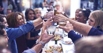 Gruppe von Menschen stoßt gemeinsam am Tisch mit den Weingläsern an und starten in die perfekte Party