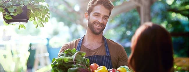 Mann flirtet mit Obstkiste auf dem Markt als Symbol für Frauen kennenlernen