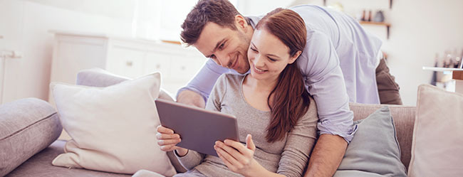Paar vergibt über Tablet auf Couch Bewertung für ElitePartner, da sie sich hier gefunden haben