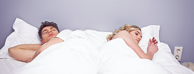 Mann und Frau liegen einander mit dem Rücken zugewandt im Bett weil sie eine kein Sex an Weihnachten haben