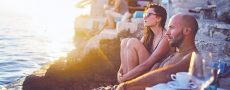 Urlaubsmythen symbolisch durch Paar im Urlaub das Sonnenuntergang an einer Klippe anschaut