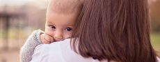 Frau zum Rücken zur Kamera hat Kind auf dem Arm das in Kamera schaut als Symbol für den Kinderwunsch in einer Beziehung