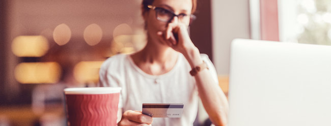 Frau sitzt unsicher vor Laptop mit Kreditkarte in der Hande symbolisch für den Schutz gegen Romance Scamming bei ElitePartner