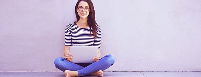 Single-Frau sitzt im Schneidersitz mit Laptop auf dem Boden und ist froh den ElitePartner Kundenservice genutzt zu haben