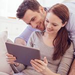 Paar vergibt über Tablet auf Couch Bewertung für ElitePartner, da sie sich hier gefunden haben