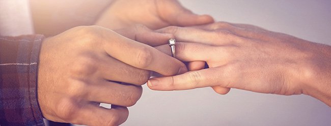 Mann macht Frau einen Heiratsantrag und steckt einen Verlobungsring an ihren Finger