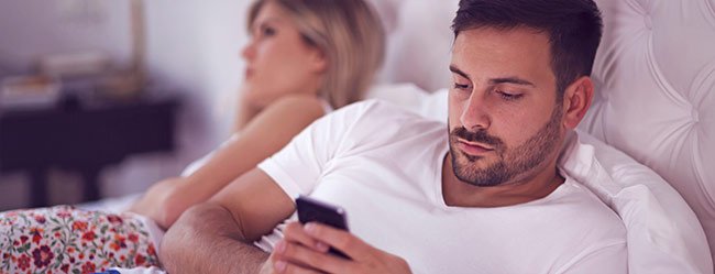 Smartphones belasten die Beziehung dargestellt durch ein Paar das im Bett jeweils vertieft ins Handy ist