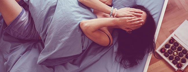 Frau mit zusammengeschlagenen Händen vor Gesicht im Bett und versucht Ex zu vergessen